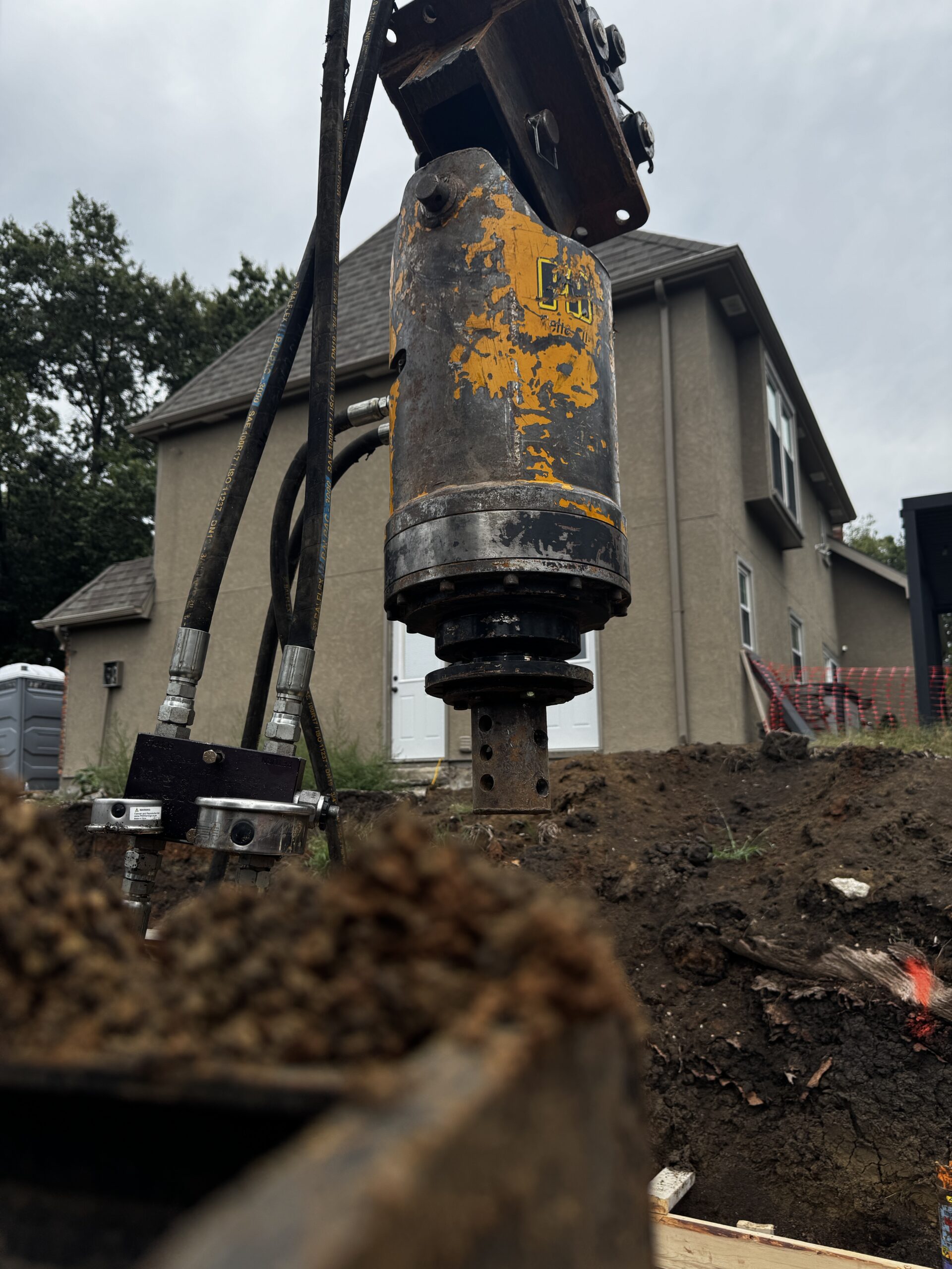 Close up of a weathered yellow and black drilling auger on a construction site with a house in the background
